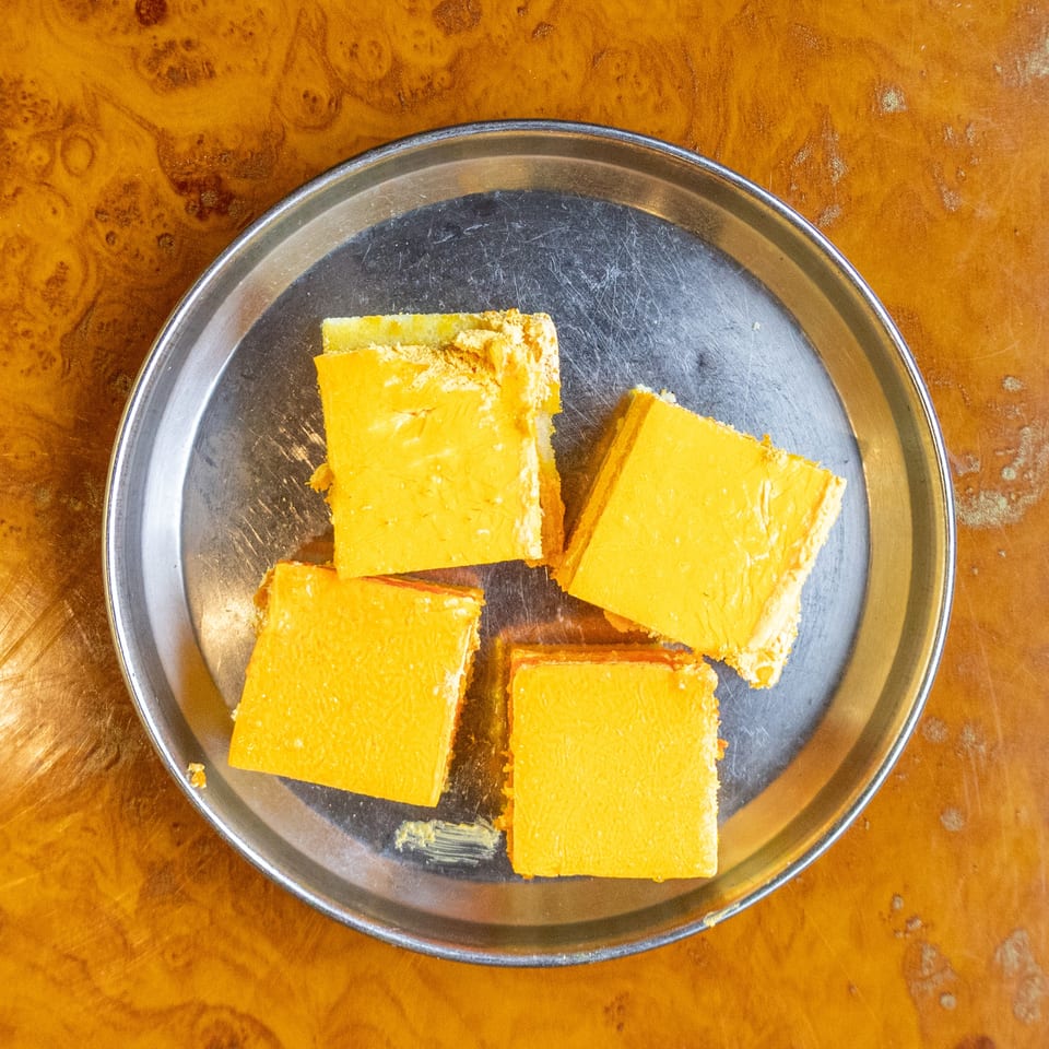 Several square slices of golden layered cake on a round metal plate atop a wooden table.
