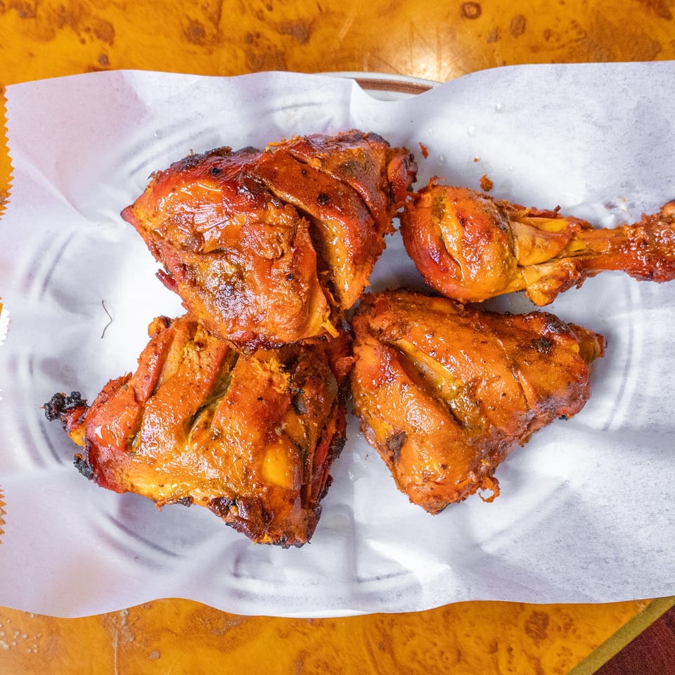 Several pieces of golden-brown roasted chicken arranged on parchment paper atop a wooden table.