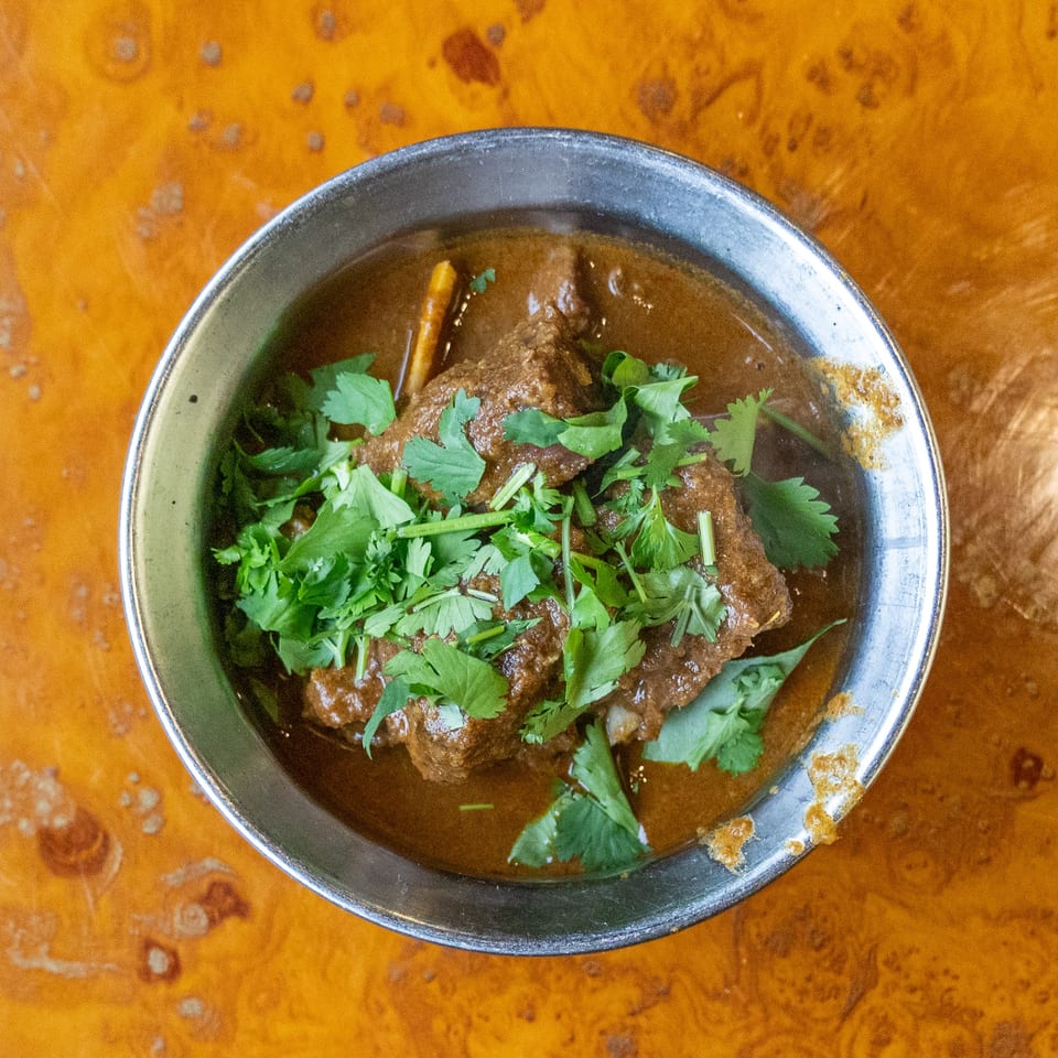 Overhead view of braised meat in dark sauce, topped with fresh cilantro, served in a metal bowl on a wooden table.