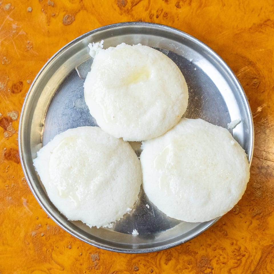 Three white steamed rice cakes arranged on a metal plate atop a polished wooden table.