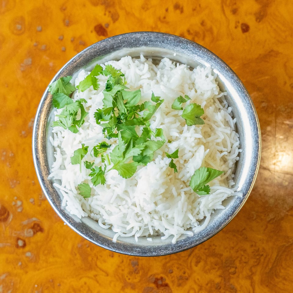 Overhead view of white rice topped with fresh cilantro in a metal bowl on a wooden table.