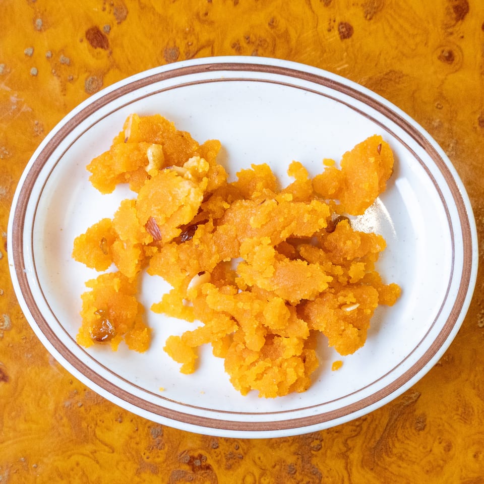 Orange sweet dessert with raisins and nuts served on a white plate atop a wooden table.