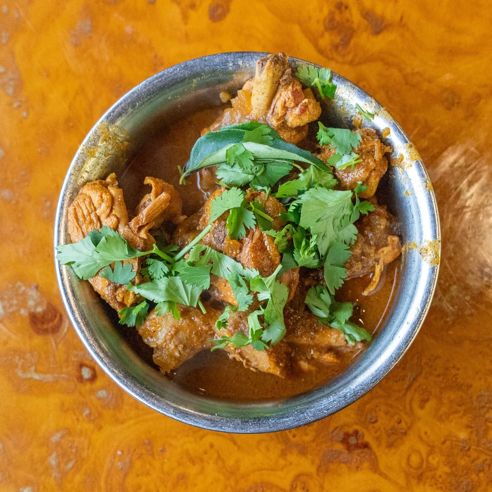 Bowl of tender meat in rich brown sauce, topped with fresh cilantro, on a rustic wooden table.